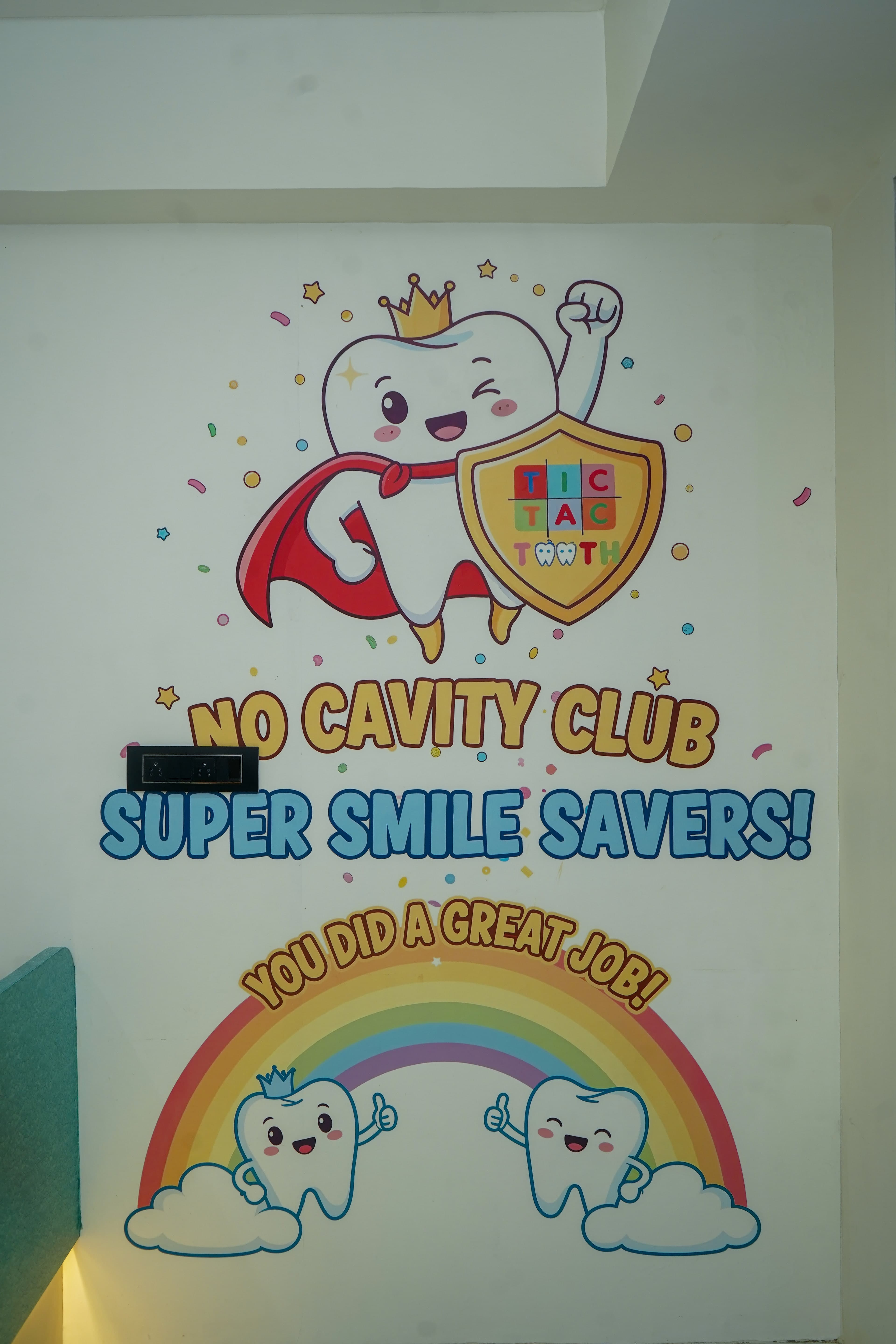 The No Cavity Club mural on the reception wall: a winking superhero tooth in a gold crown and red cape holding a shield with the Tic Tac Tooth logo, above the words No Cavity Club, Super Smile Savers, and a rainbow
